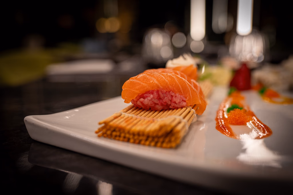 Sushi with salmon and rice elegantly presented on a white plate with sauce and garnish.