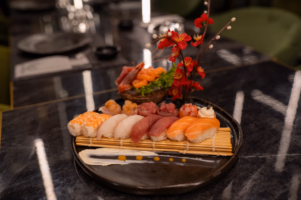 Plate of assorted sushi nigiri and sashimi garnished with red flowers on a dark marble table.